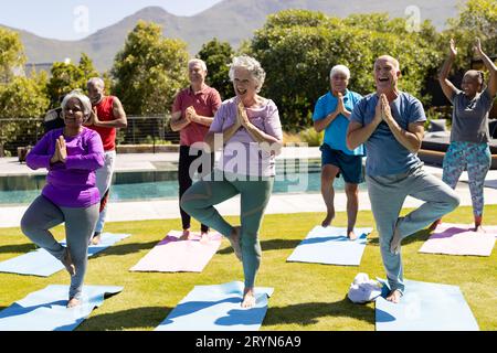 Glückliche, vielfältige ältere Freunde, die im sonnigen Garten Yoga üben Stockfoto