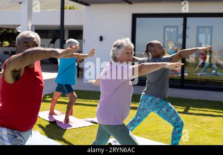 Glückliche, vielfältige ältere Freunde, die im sonnigen Garten Yoga üben Stockfoto