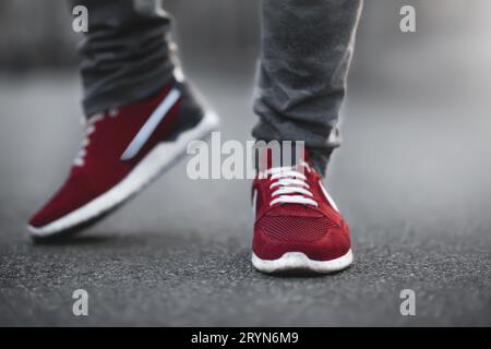 Sportliche rote Sneakers aus nächster Nähe auf Asphalt. Beine und Schuhe aus dem unteren Winkel. Stockfoto