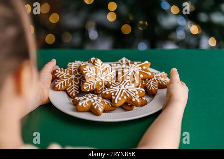 Ingwerweiskekse in Kinderhänden auf dem Hintergrund des Weihnachtsbaums. Stockfoto