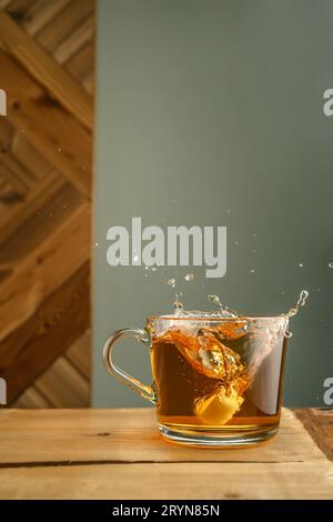 Transparenter Becher mit Tee und Spritzern auf grünem Hintergrund. Stockfoto