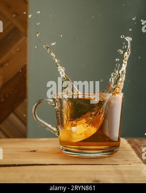 Transparenter Becher mit Tee und Spritzern auf grünem Hintergrund. Stockfoto