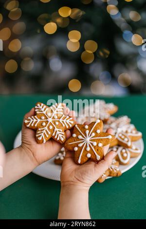 Ingwerweiskekse in Kinderhänden auf dem Hintergrund des Weihnachtsbaums. Stockfoto