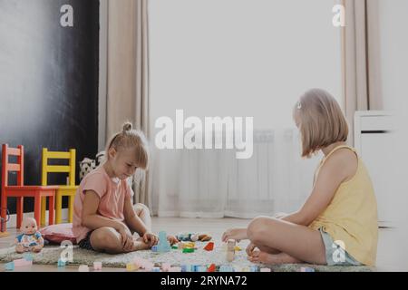 Kinder spielen mit bunten Holzspielzeugblöcken und Ziegeln. Kinder sitzen auf dem Boden im sonnigen weißen Schlafzimmer oder Kindergarten, Kindertagesstätte Spielzimmer Stockfoto