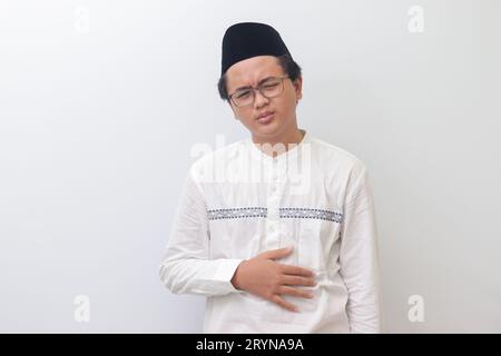 Porträt eines jungen asiatischen muslimischen Mannes, der Magenschmerzen spürt. Bauchschmerzen-Konzept. Isoliertes Bild auf weißem Hintergrund Stockfoto