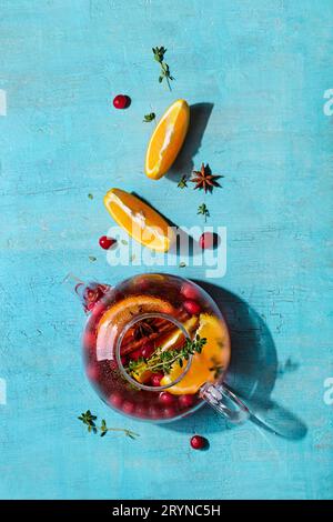 Immunitätssteigerungsgetränk. Wintertee mit Preiselbeeren, Orange, Hibiskus und Gewürzen in Glaskanne auf blauem Tisch Stockfoto