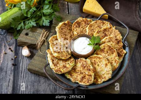 Gesundes Sommeressen, Zucchini-Krapfen. Vegetarische Zucchini-Pfannkuchen mit Käse, serviert mit Sauerrahm auf einem rustikalen Holztisch Stockfoto