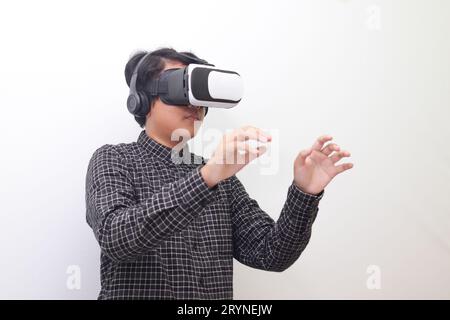 Porträt eines asiatischen Mannes in einem schwarzen karierten Hemd mit Virtual Reality (VR) Brille und dem Versuch, etwas vor ihm zu halten. Isoliertes Bild auf weißem BA Stockfoto