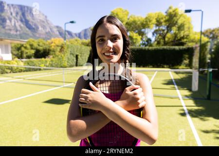 Porträt einer birassischen jungen Frau, die auf dem Tennisplatz einen lächelnden Tennisschläger hält Stockfoto