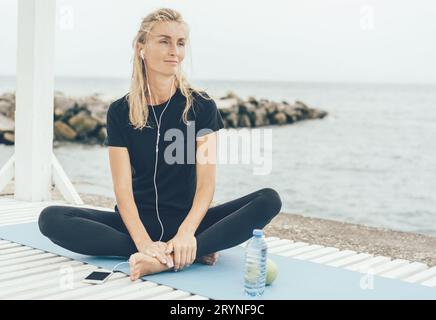 Frau, die sich nach dem Sport-Training draußen ausruhte und Musik oder Meditation über Kopfhörer hörte. Stockfoto