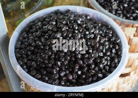 Schneidet schwarze Oliven mit einem Löffel in einer Schüssel, Stockfoto
