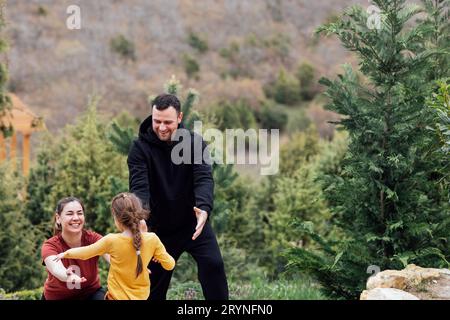 Ein kleines Mädchen in gelben Kleidern rennt zu ihren fröhlichen Eltern. Ein junges lächelndes Paar streckt ihre Hände ihrer süßen Tochter aus. Stockfoto