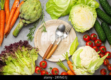 Verschiedene rohe Lebensmittel: Gemüse, Rindfleisch, Fischlachs und leerer Teller in der Mitte, heller rustikaler Steintisch mit Blick auf die Tischplatte Stockfoto