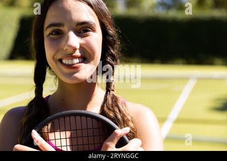 Nahaufnahme einer lächelnden, birassischen jungen Frau mit Tennisschläger auf dem Tennisplatz am sonnigen Tag Stockfoto