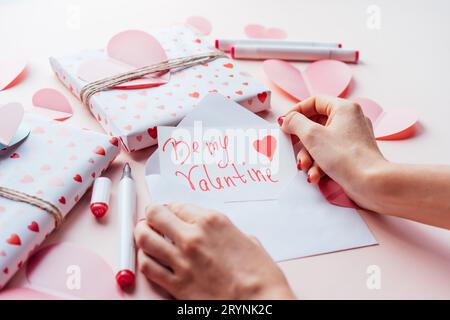 Frauenhände wickeln eine Notiz in einen Umschlag mit den Worten BE MY VALENTINE. Stockfoto