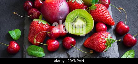 Erdbeere, Kirsche, Kiwi und Pfirsiche auf schwarzem Schieferteller. Lang Stockfoto