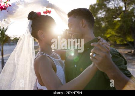 Frisch verheiratetes junges Paar, das bei Sonnenuntergang romantisch am Strand tanzt Stockfoto