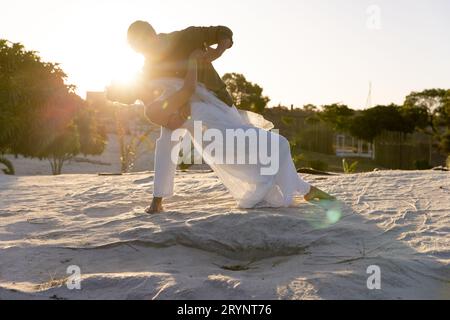 Kaukasisches frisch verheiratetes Paar tanzt am Sandstrand gegen den klaren Himmel bei Sonnenuntergang, Kopierraum Stockfoto