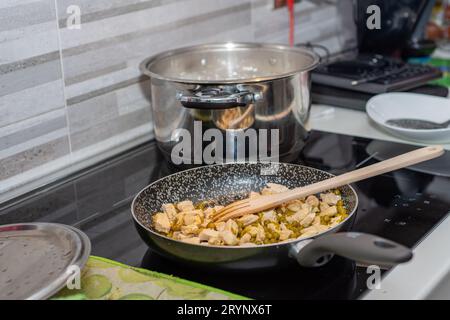 Huhn und Erbsen kochen in einer Pfanne auf einem Induktionskochfeld. Typisch italienische Küche Stockfoto