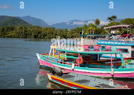 Blick auf farbenfrohe Ausflugsboote im Wasser, die an einem Pier auf Touristen warten, mit grünen Bergen im Hintergrund, Paraty, Brasilien, Stockfoto