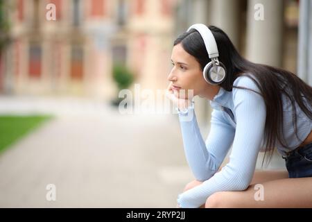 Profil einer entspannten Frau mit Kopfhörern, die Podcast auf der Straße hört Stockfoto