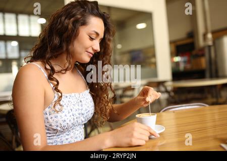 Zufriedene Frau, die in einem Restaurant sitzt und Kaffee rührt Stockfoto