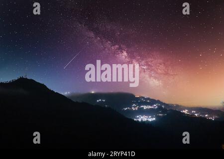 Nächtliche Aufnahme mit Nebel, der über Hügel mit einem Dorf in der Ferne rollt und unberührte Hügel von darjeeling, shimla, manali, landsdowne zeigt Stockfoto