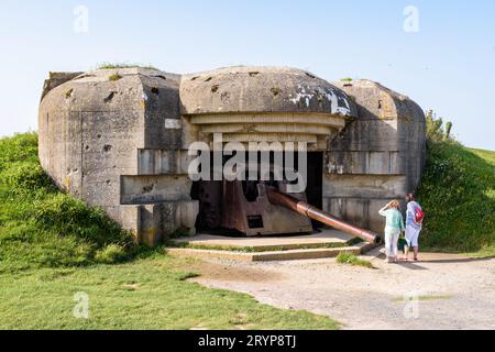 Touristen beobachten die 150-mm-Kanone in einem Bunker in der Longues-sur-Mer-Batterie in der Normandie, einer deutschen Küstenartillerie-Batterie, die Teil der Atlantischen Mauer ist. Stockfoto