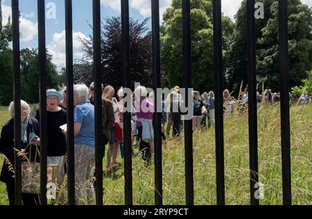 Die Schlange für das Hospital of St Cross und Almshouse of Noble Poverty, das jährliche Sommerfest findet seit über 150 Jahren statt. Lokale Besucher stehen in der Warteschlange, um Zutritt zu erhalten. Durch den Metallzaun des Anwesens gesehen. Winchester, Hampshire, England, 25. Juni 2022. HOMER SYKES AUS DEN 2020ER JAHREN Stockfoto