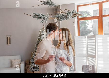 Nahaufnahme eines liebevollen, jungen, lustigen Paares mit Gläsern Champagner zu Weihnachten. Liebende sehen sich an, umarmen, lachen, taktilisch. Trendige Inte Stockfoto