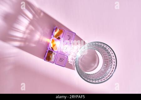 Helle Pillenbox mit verschiedenen Pillen und Vitaminen neben einem Glas Wasser. Stockfoto