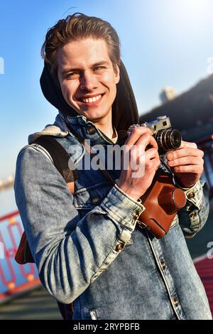 Junger fröhlicher Mann Fotograf, der mit der Kamera fotografiert Stockfoto