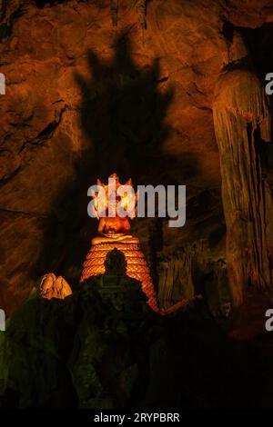 Meditierende Buddha-Statue mit Naga-Schlange (mehrköpfige Königskobra, Mucalinda) und Schatten an der Wand in der Tham Khao Luang Höhle in Phetchaburi, Thailand. Stockfoto