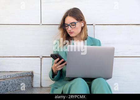 Geschäftsfrau, die auf einer Treppe vor dem Bürogebäude sitzt, während sie ihr Smartphone benutzt Stockfoto