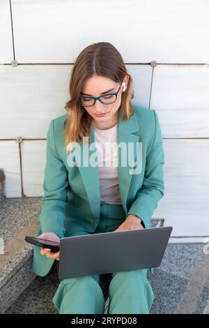 Geschäftsfrau, die auf einer Treppe vor dem Bürogebäude sitzt, während sie ihr Smartphone benutzt Stockfoto