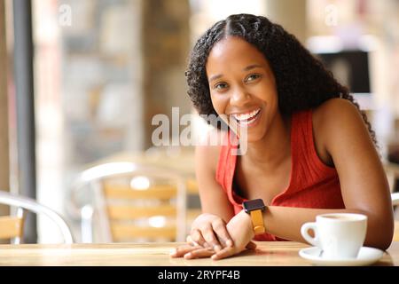 Glückliche schwarze Frau lacht, die auf einer Bar-Terrasse in die Kamera schaut Stockfoto