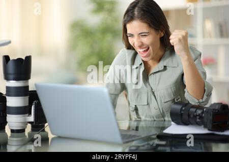 Begeisterter Fotograf feiert gute Ergebnisse beim Ansehen von Notebook-Inhalten zu Hause Stockfoto