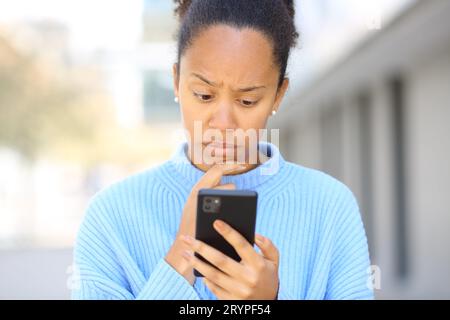 Vorderansicht Porträt einer besorgten schwarzen Frau, die auf der Straße das Telefon überprüft Stockfoto