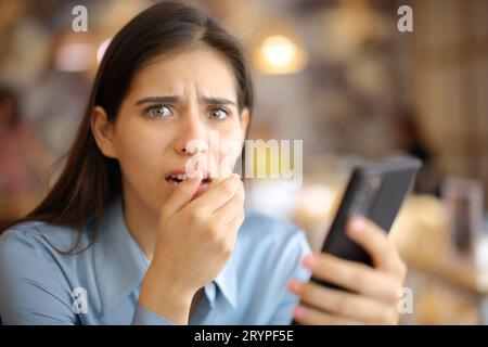 Verängstigte Frau, die in einer Bar das Telefon hält und die Kamera ansieht Stockfoto