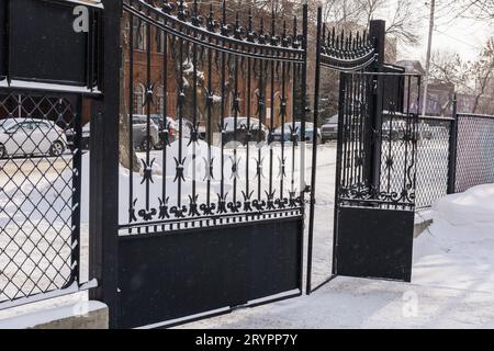 Altes Eisentor mit freigeschaltetem Eisen, schneebedeckte Szenen, die fallen und Schnee auf Metall liegen. Winterstadt Stockfoto