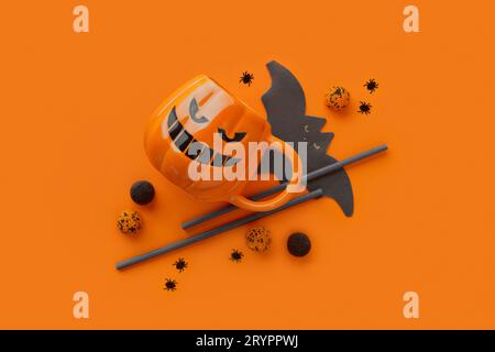Kürbisbecher, Gummibärchen, Strohhalme, Fledermausservietten auf orangem Hintergrund. Halloween-Feier-Konzept Stockfoto