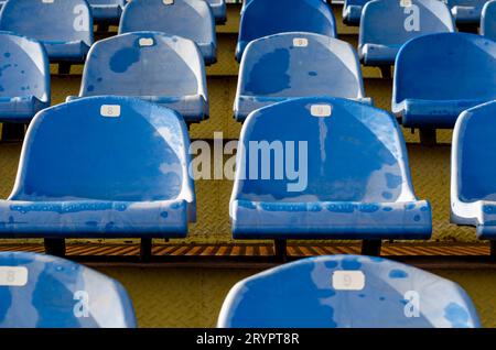 Reihen identischer nassblauer Sitze in den leeren Stadiontribünen Stockfoto