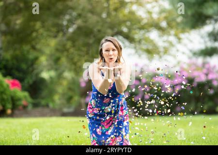 Freudige Frau, die Konfetti aus den Händen bläst Stockfoto
