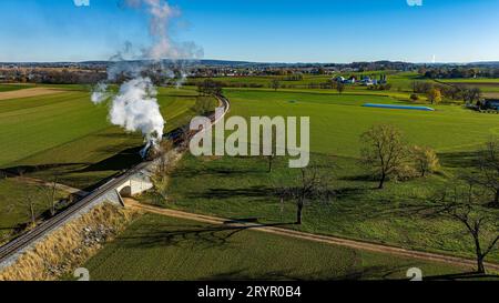 Ein Luftblick auf einen stromlinienförmigen Dampfzug, der an einem Herbsttag um eine Kurve fährt und Rauch bläst Stockfoto