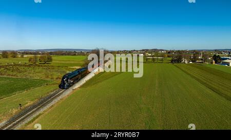 Ein Blick aus der Luft auf einen stromlinienförmigen Dampfzug, der an einem Herbsttag durch fruchtbare Ackerflächen fährt Stockfoto