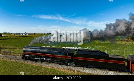 Ein Blick von der Luft auf eine antike stromlinienförmige Dampflokomotive, die durch die Blase von schwarzem Rauch fährt, durch die Landschaft an einem Herbsttag Stockfoto