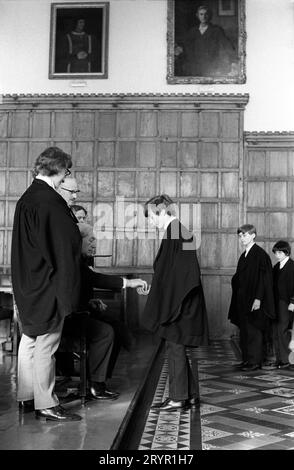 Eton College, Kings Scholars stellen sich zusammen und sammeln ihr jährliches traditionelles 3D-Stück vom College Provost. Diese Tradition, die als Threepenny Day bekannt ist, ist 400 Jahre alt. Die jährliche Verteilung erfolgte nach dem Mittagessen in der College Hall durch den Provost Harold Caccia (Provost 1965–1977) und war auf die siebzig Könige Gelehrten beschränkt. Eton, Windsor, Berkshire, England, 27. Februar 1975. 1970ER JAHRE UK HOMER SYKES Stockfoto