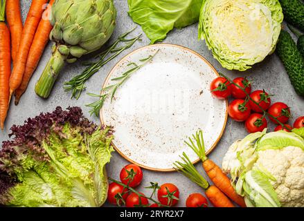 Verschiedene rohe Lebensmittel: Gemüse, Rindfleisch, Fischlachs und leerer Teller in der Mitte, heller rustikaler Steintisch mit Blick auf die Tischplatte Stockfoto