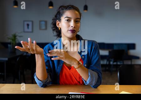 Glückliche, birassistische Geschäftsfrau, die während eines Videoanrufs am Schreibtisch zuhört Stockfoto