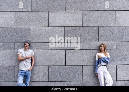 Das hübsche Paar zeigt weg und lächelt, steht an der grauen Wand. Stockfoto